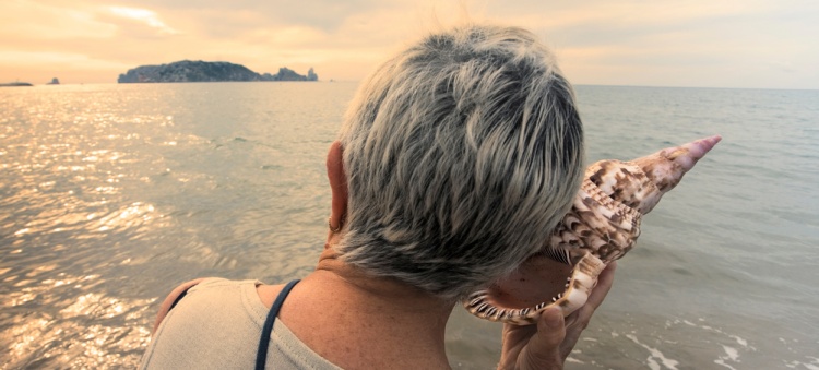 Dame âgée écoutant un coquillage sur la plage